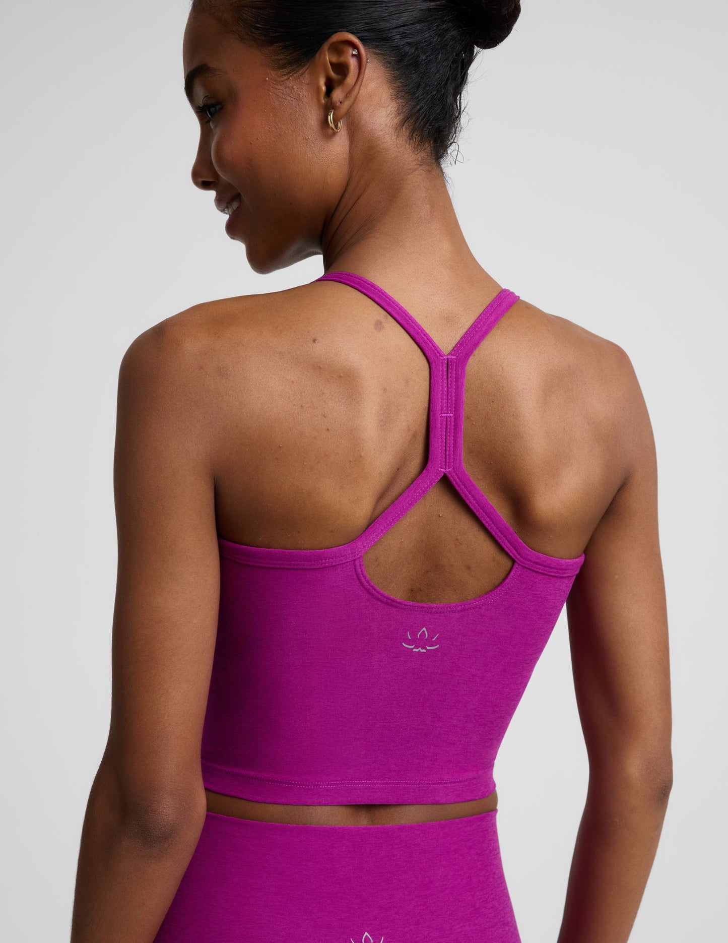Woman wearing a purple racerback cropped tank and biker shorts against a plain background.