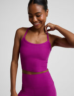 Woman wearing a purple racerback cropped tank and biker shorts against a plain background.