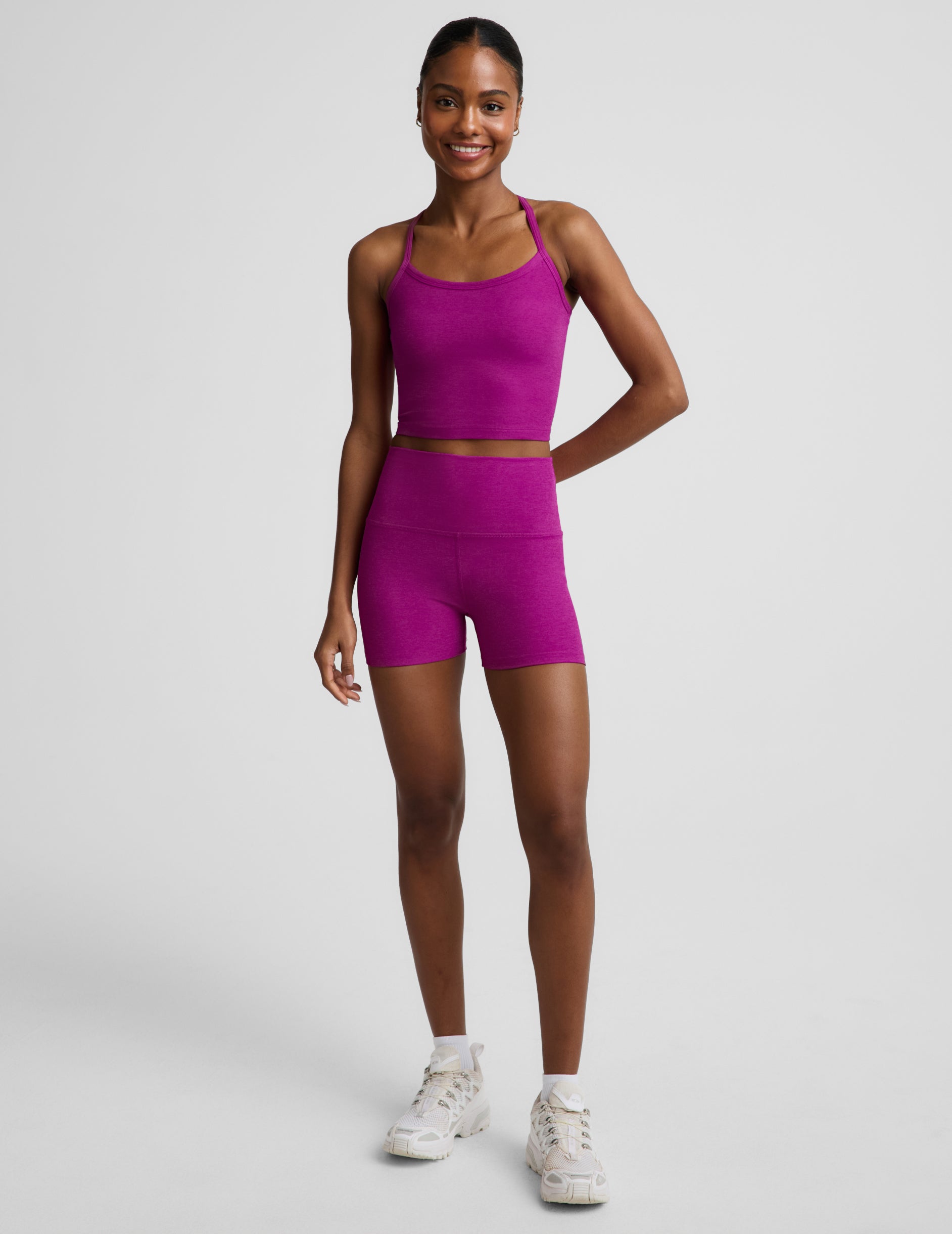 Woman wearing a purple racerback cropped tank and biker shorts against a plain background.