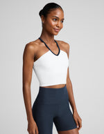 Woman wearing a white v-neck strappy cropped tank and blue biker shorts against a plain background.