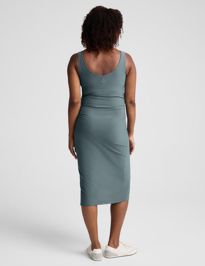 Pregnant woman wearing a green maternity midi length tank dress with a front side slit against a plain background.