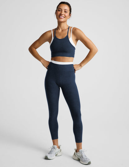 Woman wearing a navy layered bra and leggings against a plain background.