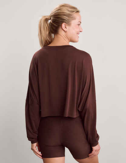 Woman wearing a brown long sleeve top and brown biker shorts against a plain background.