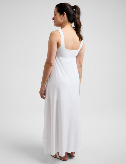 Pregnant woman wearing a white maxi dress against a plain background.