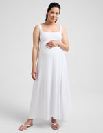 Pregnant woman wearing a white maxi dress against a plain background.