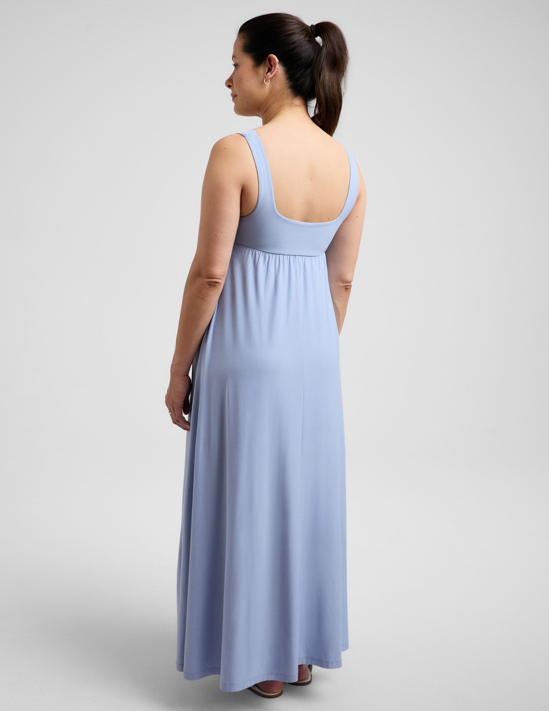 Pregnant woman wearing a blue maxi dress against a plain background.
