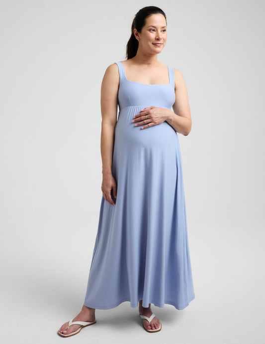 Pregnant woman wearing a blue maxi dress against a plain background.