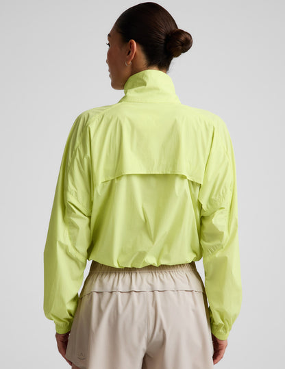 Woman wearing a yellow quarter-zip jacket and neutral colored shorts against a plain background.