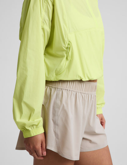Woman wearing a yellow quarter-zip jacket and neutral colored shorts against a plain background.