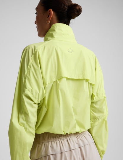 Woman wearing a yellow quarter-zip jacket and neutral colored shorts against a plain background.