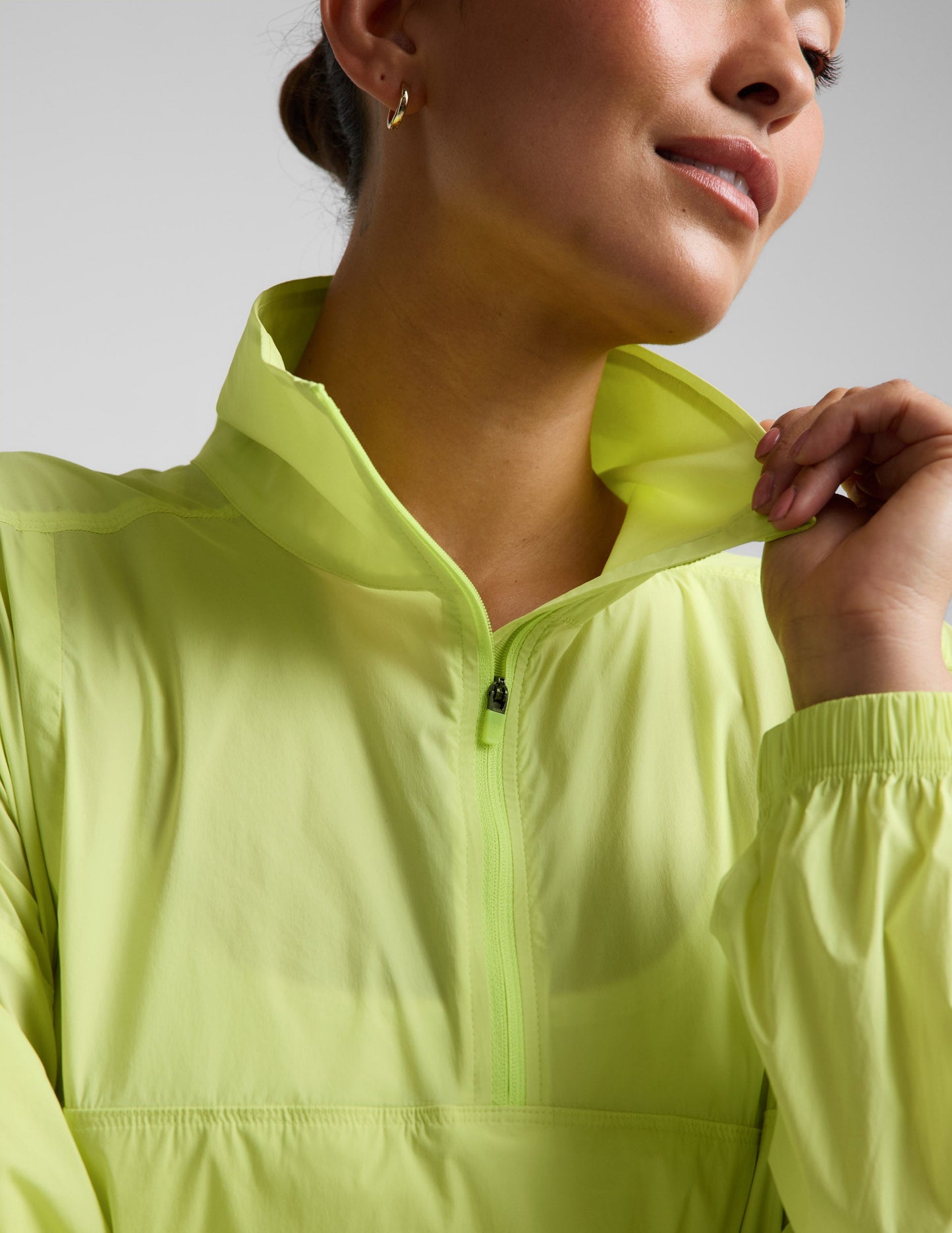 Woman wearing a yellow quarter-zip jacket and neutral colored shorts against a plain background.