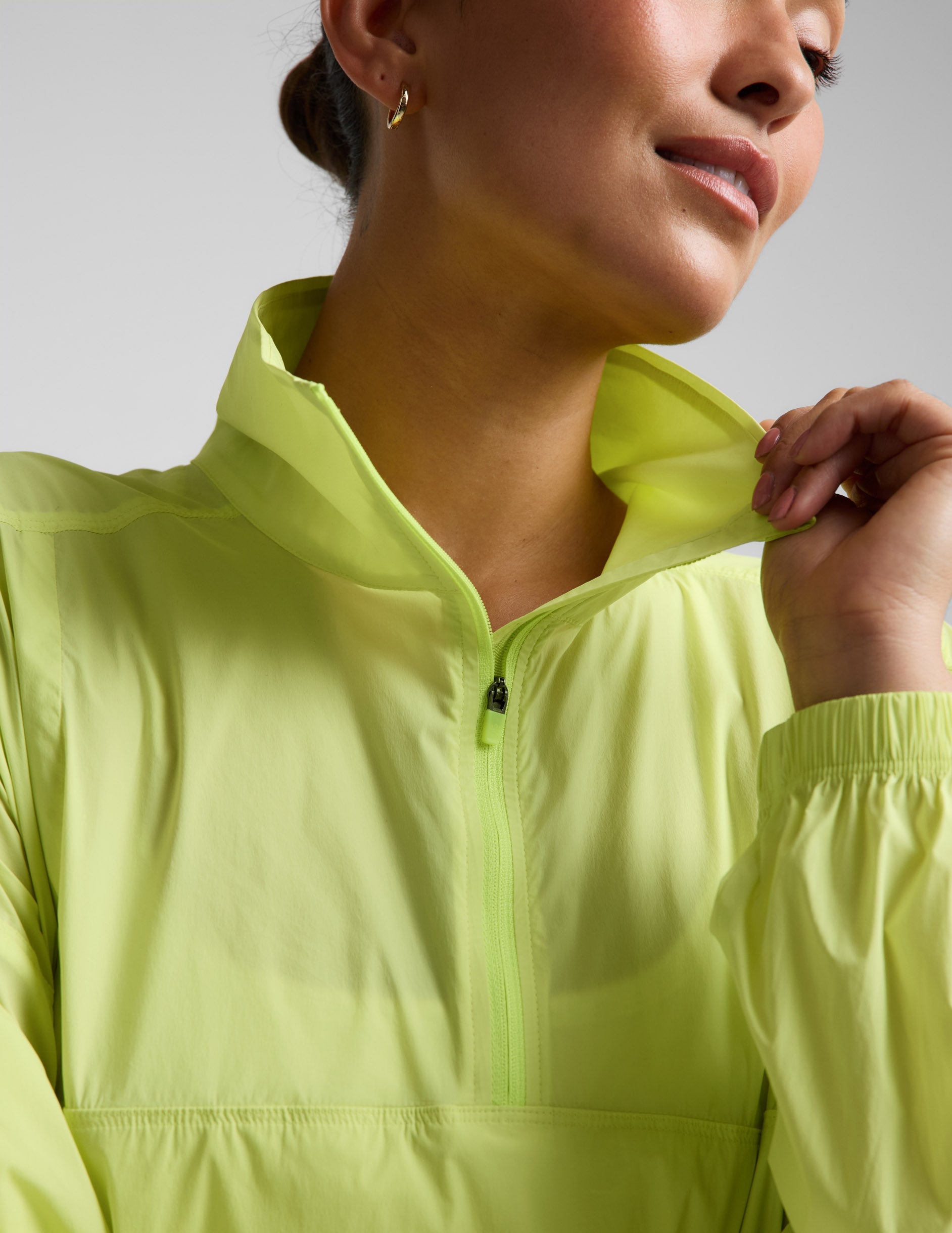 Woman wearing a yellow quarter-zip jacket and neutral colored shorts against a plain background.