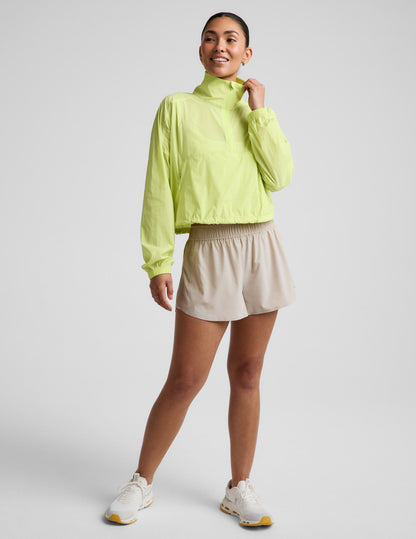Woman wearing a yellow quarter-zip jacket and neutral colored shorts against a plain background.