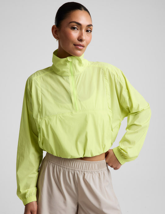 Woman wearing a yellow quarter-zip jacket and neutral colored shorts against a plain background.