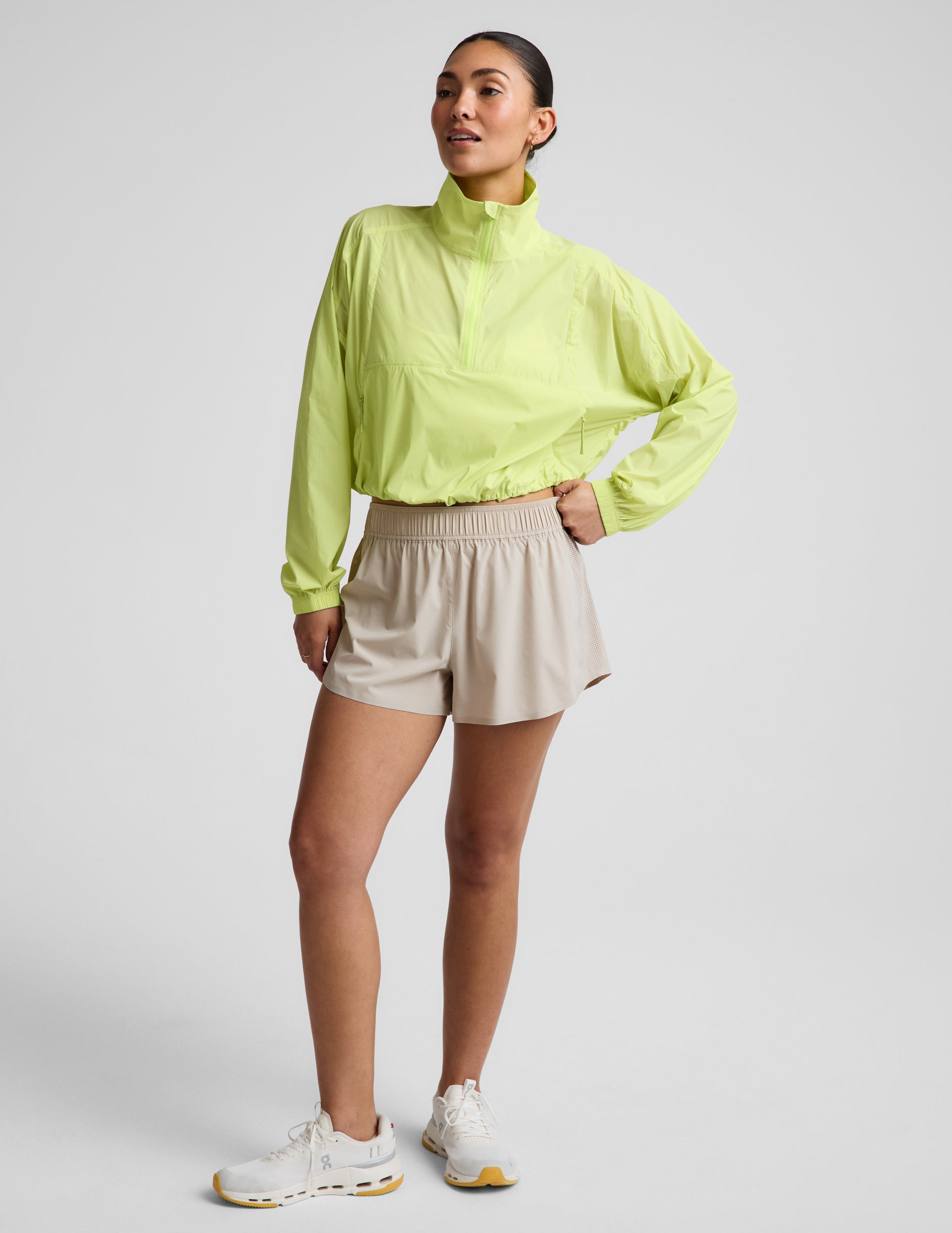 Woman wearing a yellow quarter-zip jacket and neutral colored shorts against a plain background.
