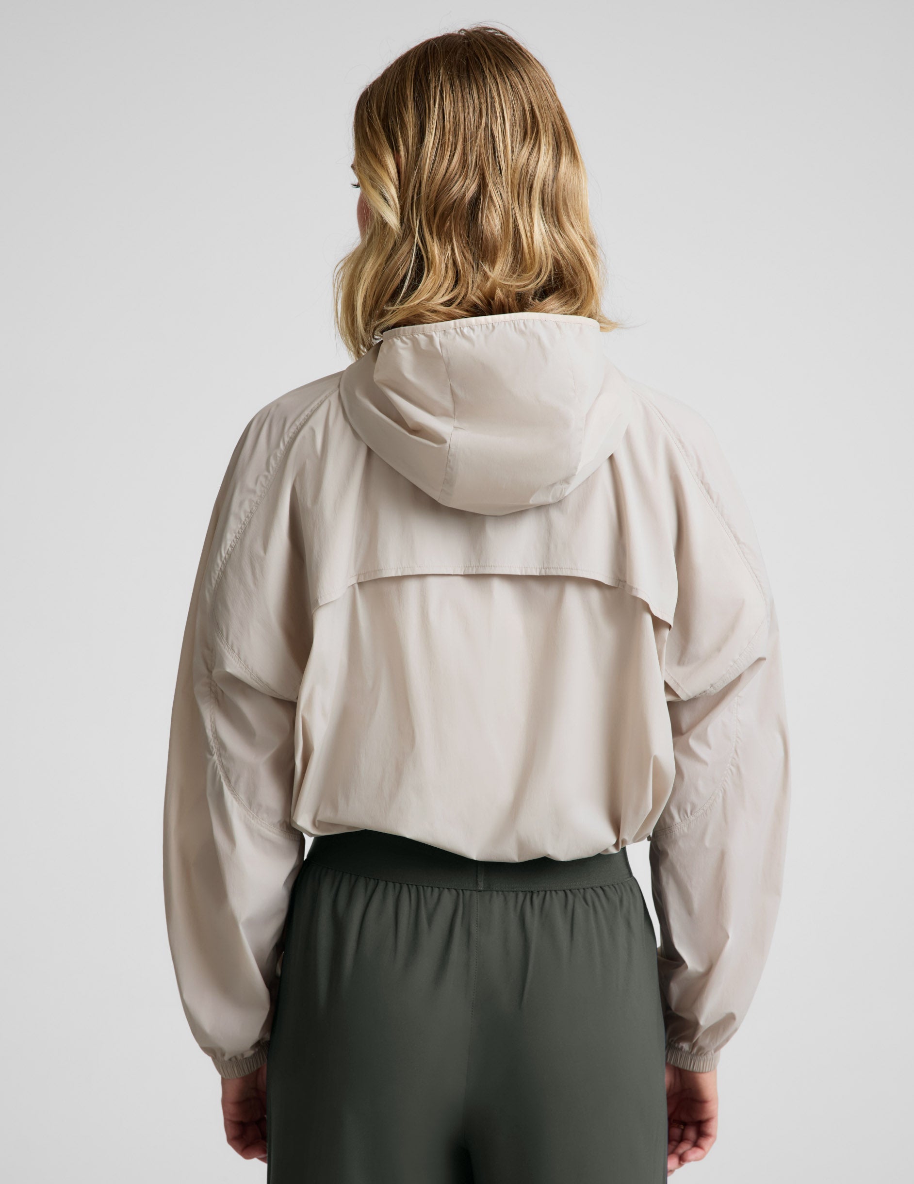 Woman wearing a beige jacket and green pants against a plain background.