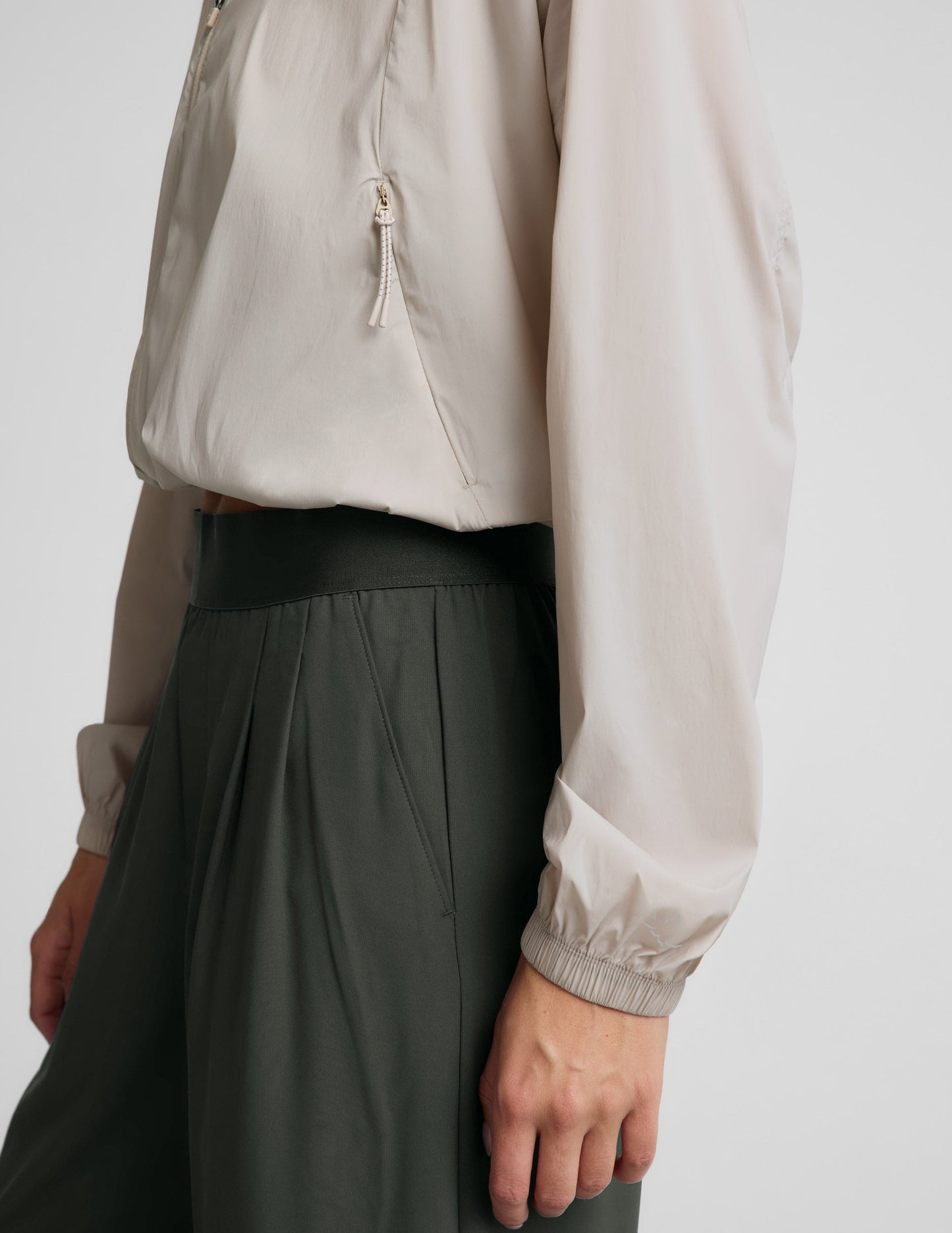 Woman wearing a beige jacket and green pants against a plain background.