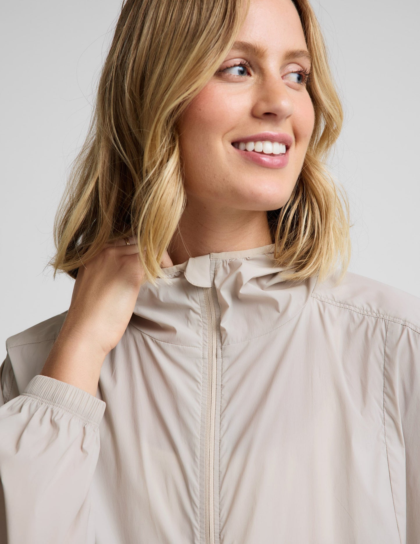 Woman wearing a beige jacket and green pants against a plain background.