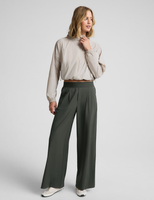 Woman wearing a beige jacket and green pants against a plain background.