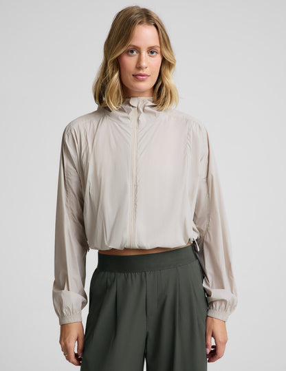 Woman wearing a beige jacket and green pants against a plain background.