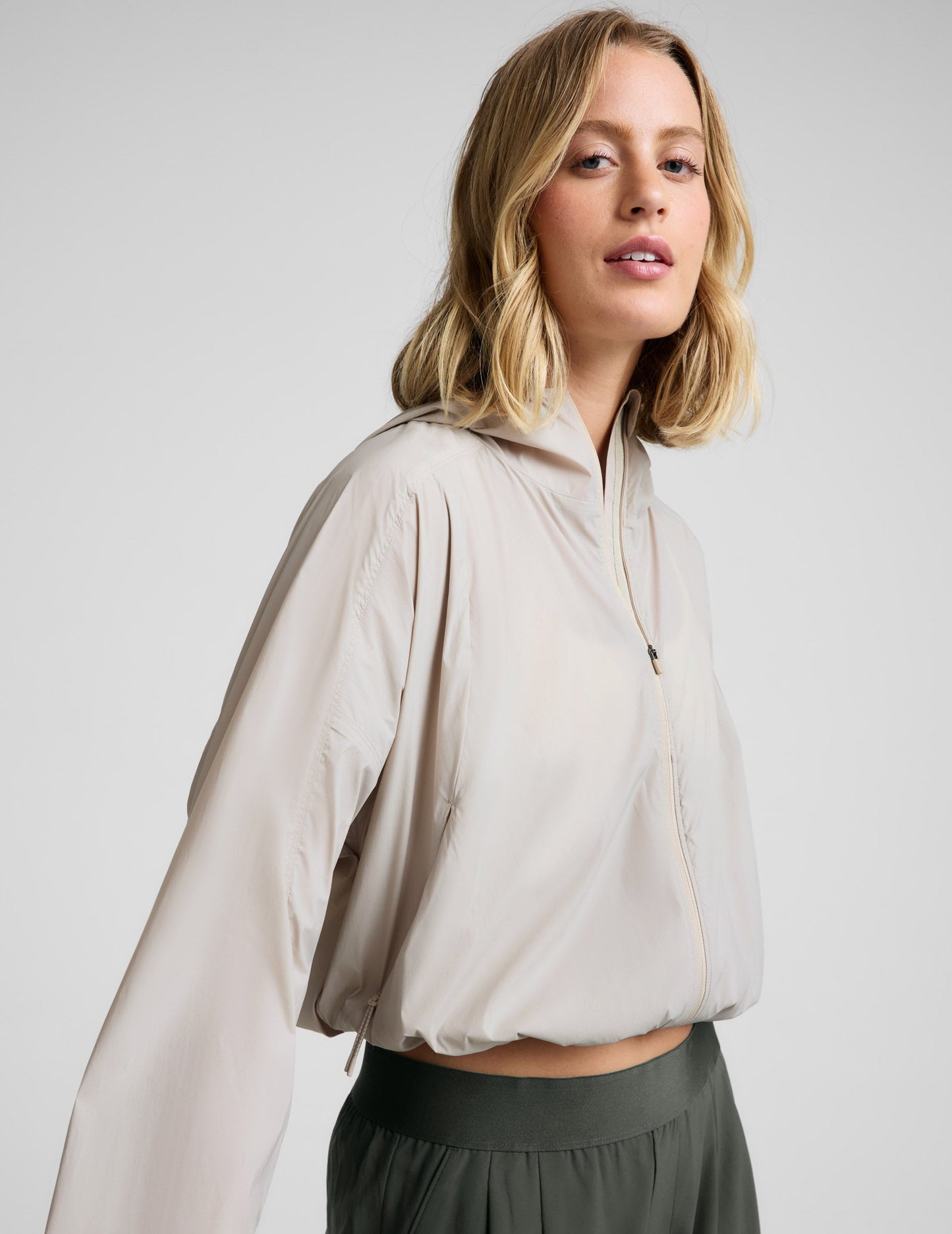 Woman wearing a beige jacket and green pants against a plain background.