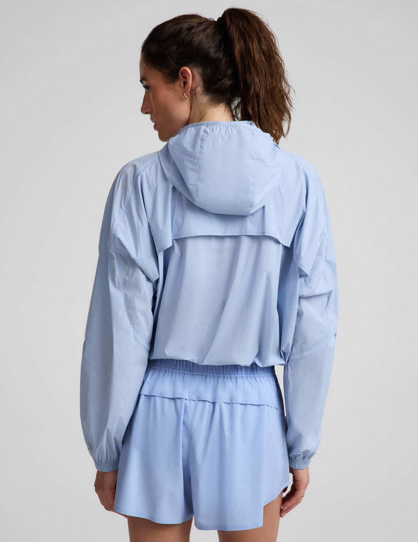 Woman wearing a light blue jacket and blue shorts against a plain background.