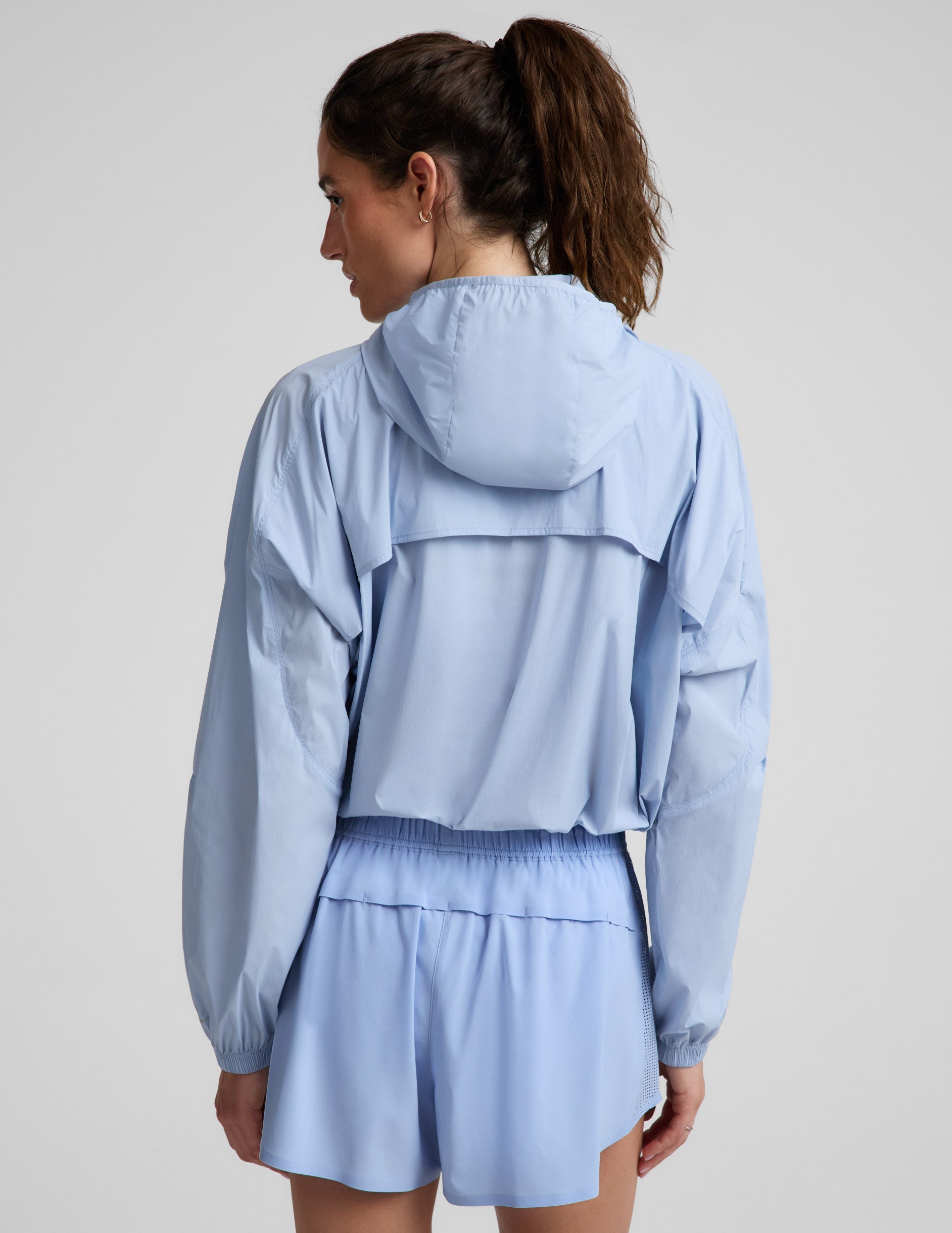 Woman wearing a light blue jacket and blue shorts against a plain background.