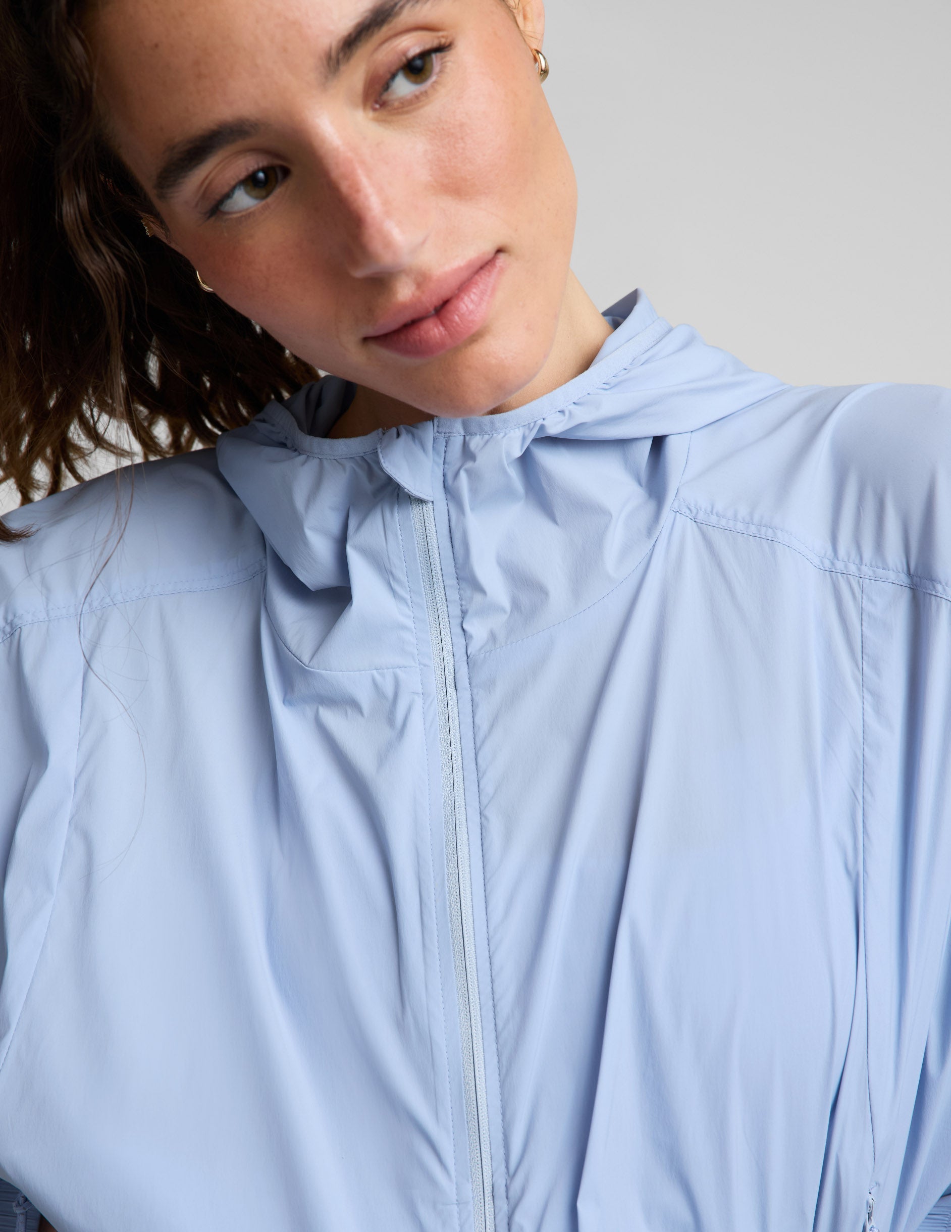 Woman wearing a light blue jacket and blue shorts against a plain background.