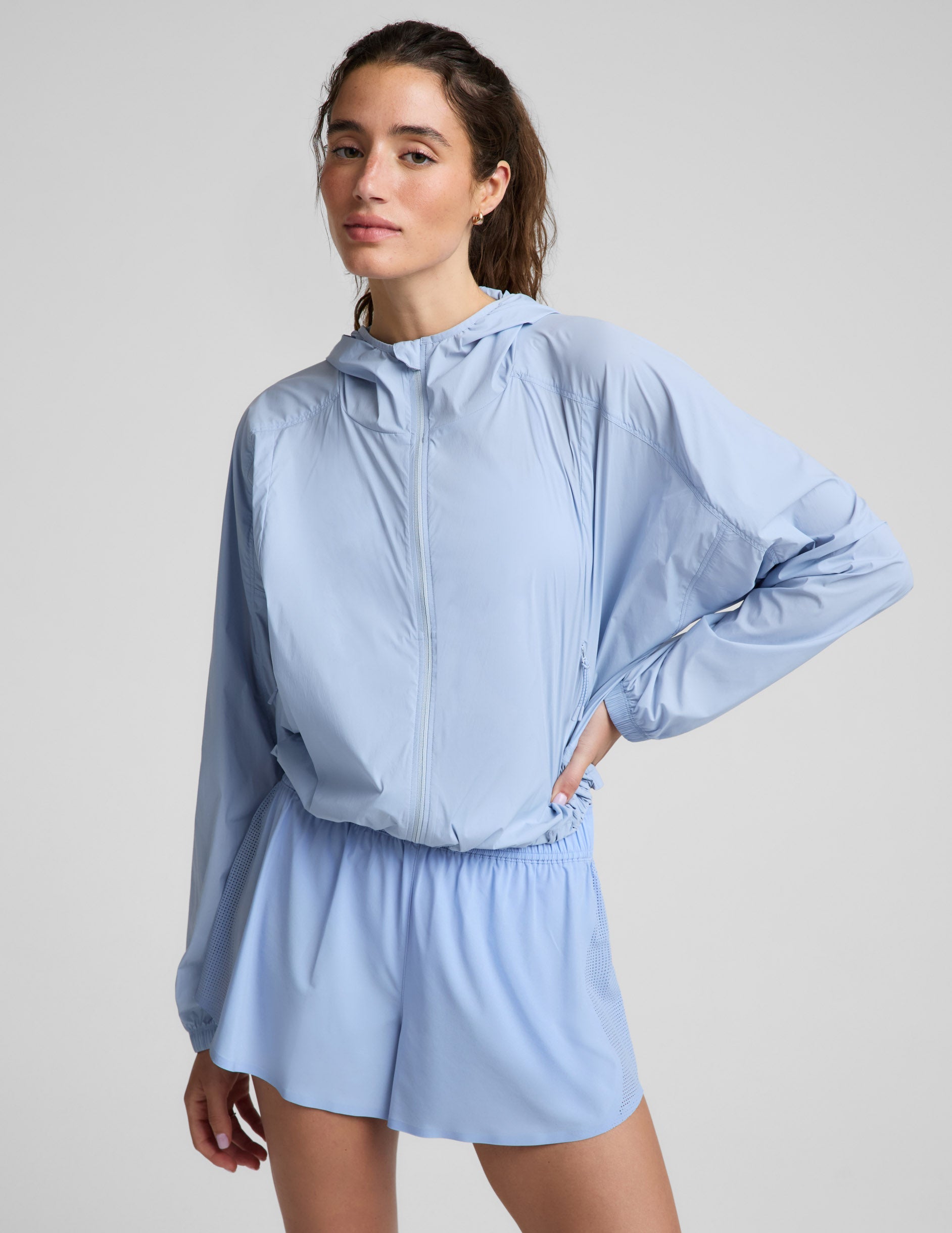 Woman wearing a light blue jacket and blue shorts against a plain background.