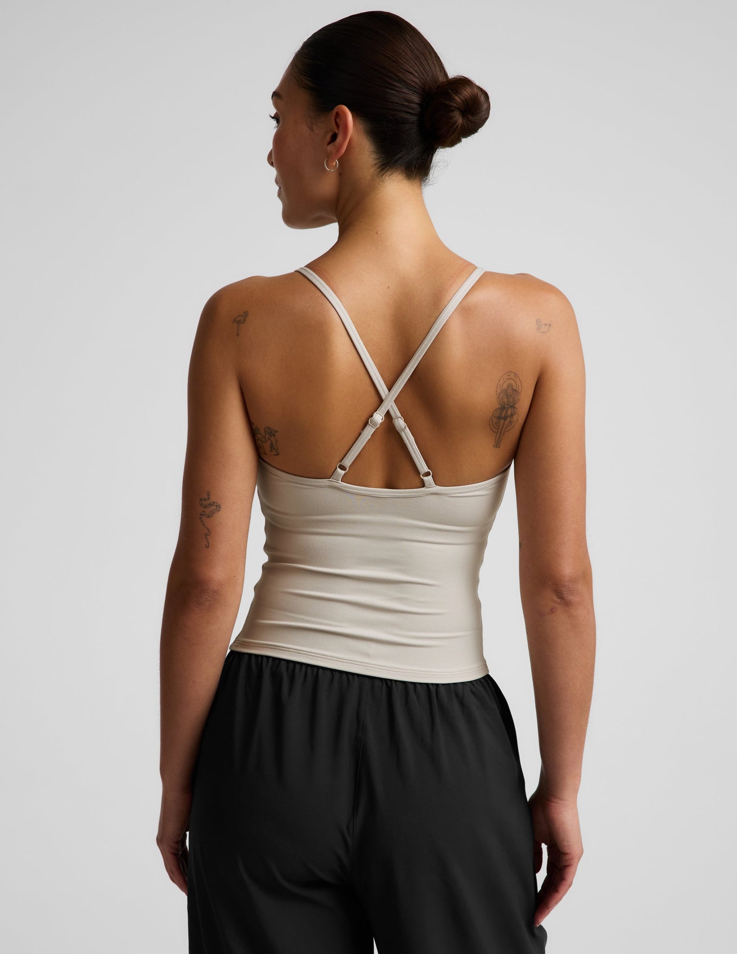 Woman wearing a beige cowl neck tank top and black trousers against a plain background.