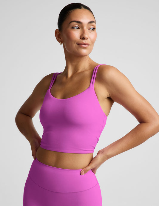 Woman wearing a purple cropped tank and purple biker shorts against a plain background.