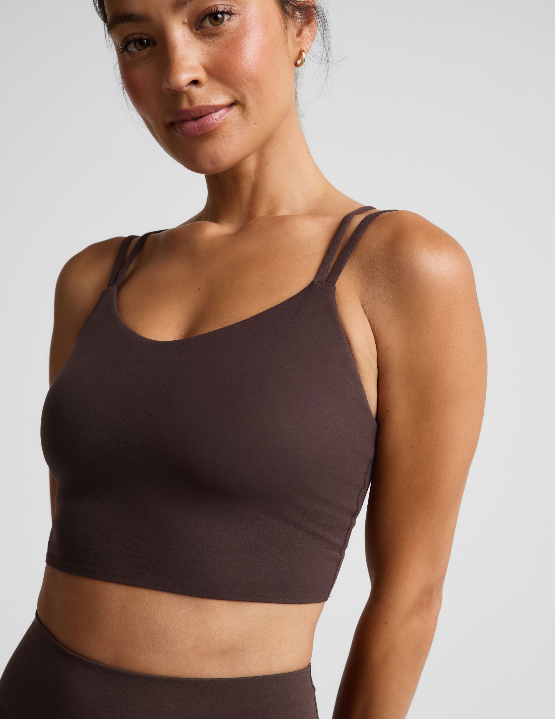 Woman wearing a brown cropped tank and midi leggings on an plain studio background.