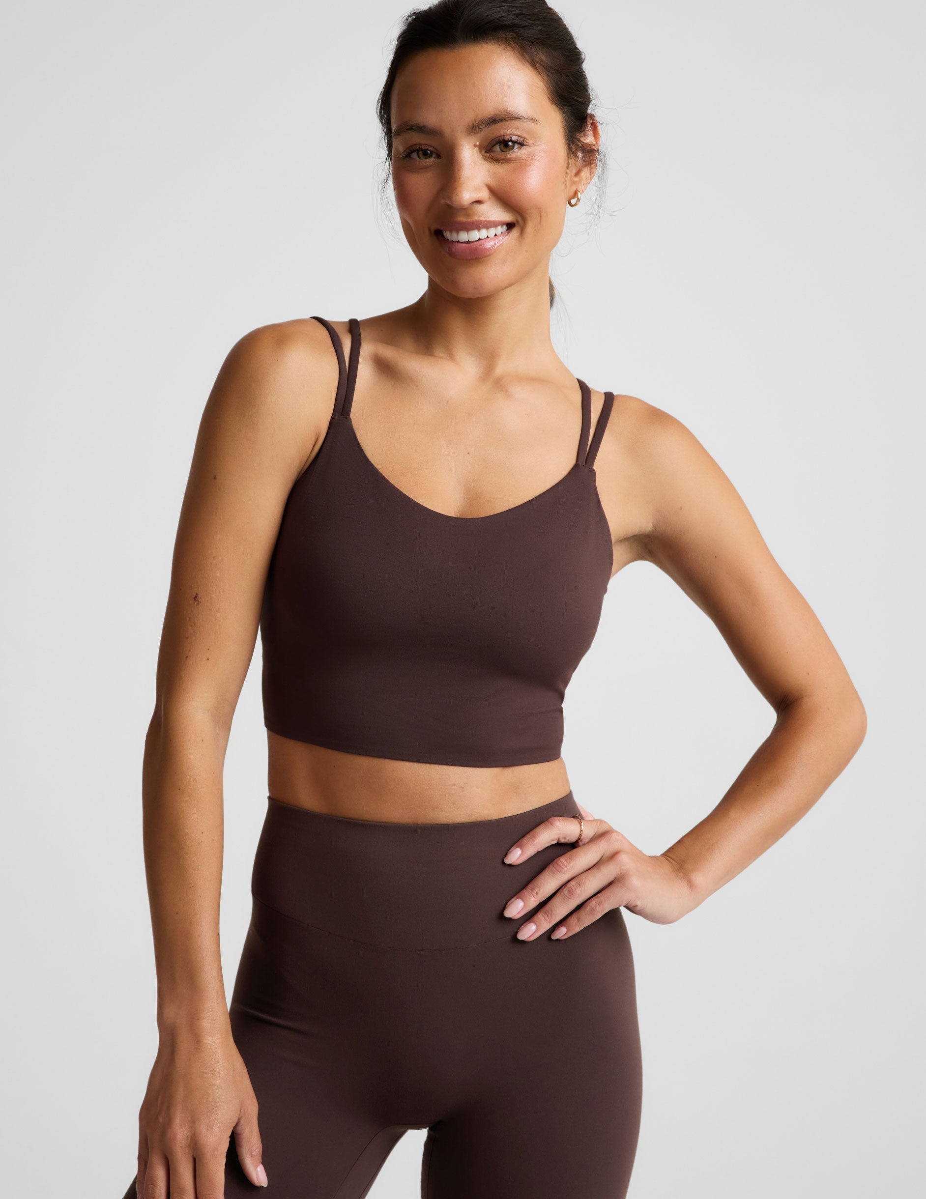Woman wearing a brown cropped tank and midi leggings on an plain studio background.