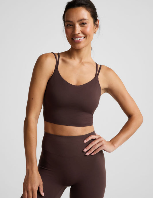Woman wearing a brown cropped tank and midi leggings on an plain studio background.