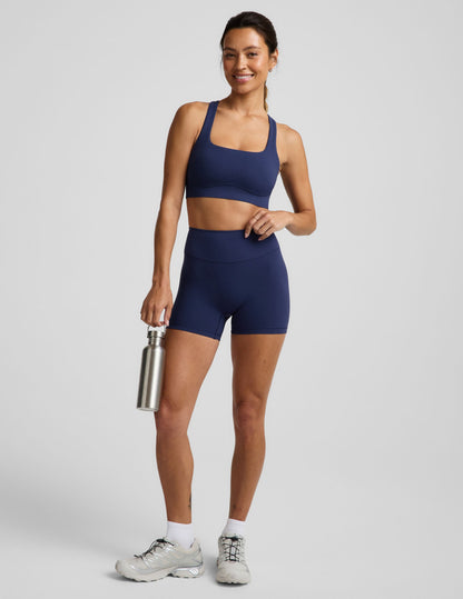 Woman wearing a blue sports bra and blue biker shorts against a plain background.