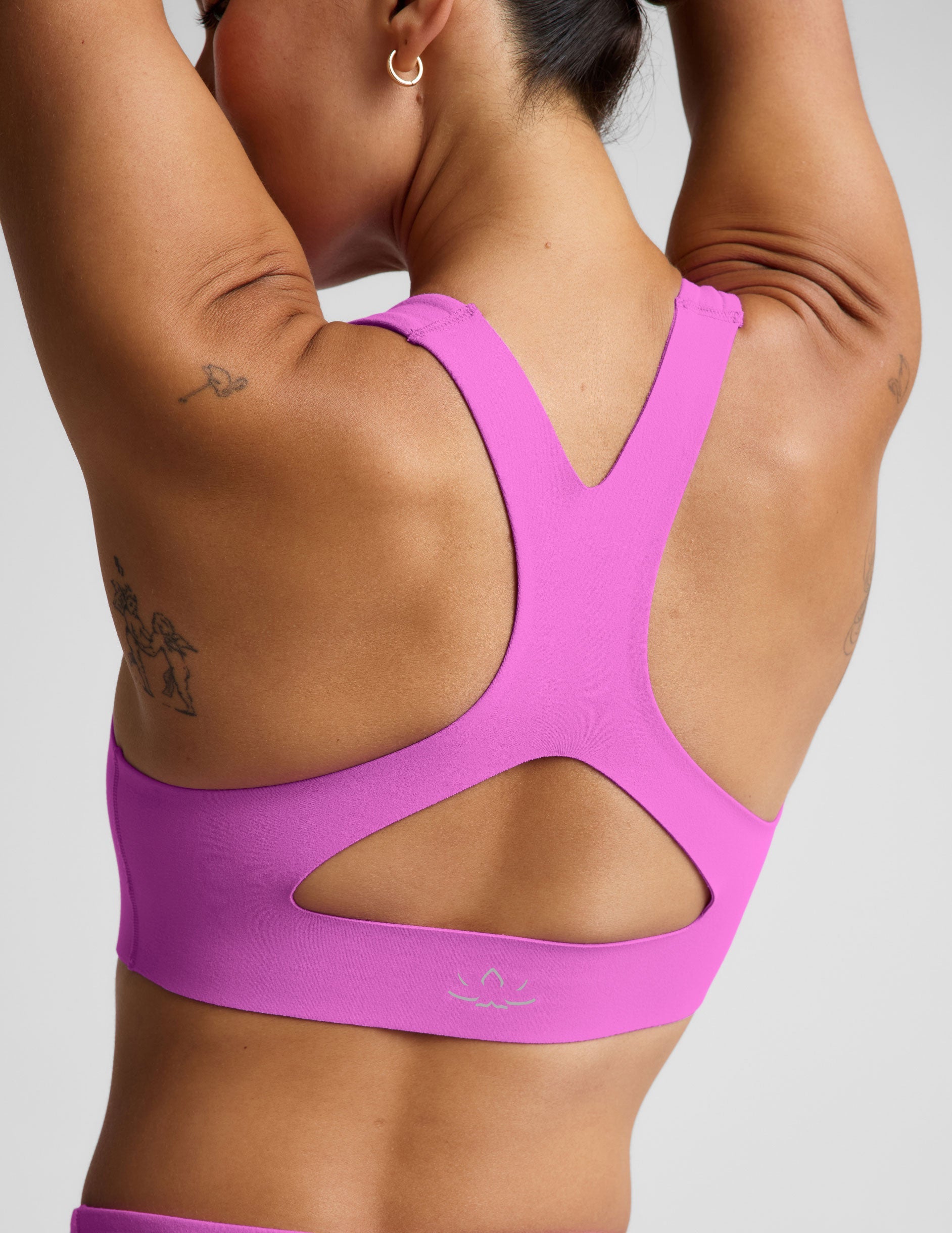 Woman wearing a purple sports bra and purple midi length leggings against a plain studio background.