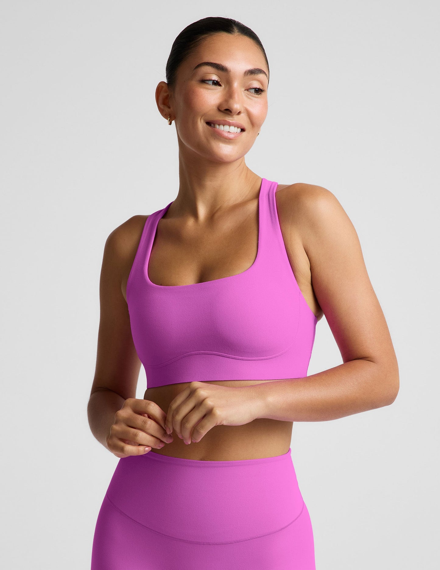 Woman wearing a purple sports bra and purple midi length leggings against a plain studio background.