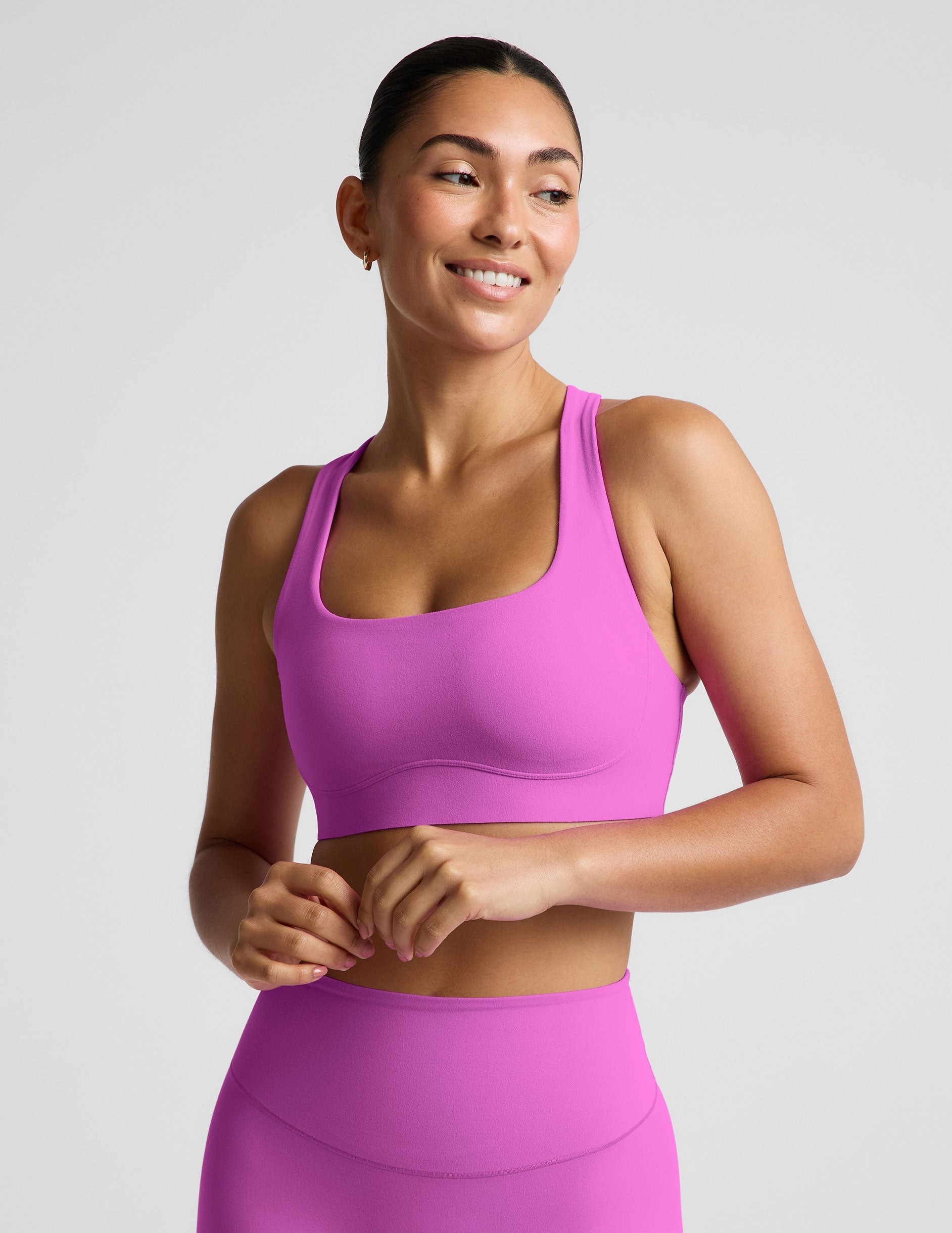 Woman wearing a purple sports bra and purple midi length leggings against a plain studio background.