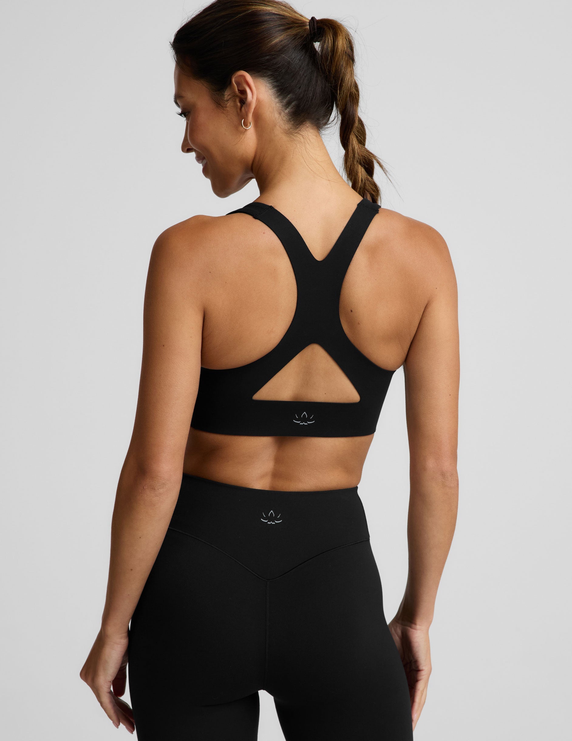 A woman in a black sports bra and black midi length leggings against a plain background.