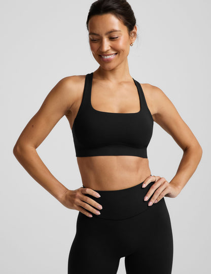 A woman in a black sports bra and black midi length leggings against a plain background.