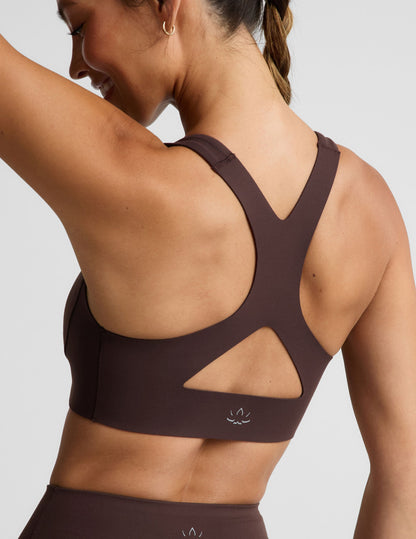 Woman wearing a brown sports bra and brown biker shorts against a plain background.