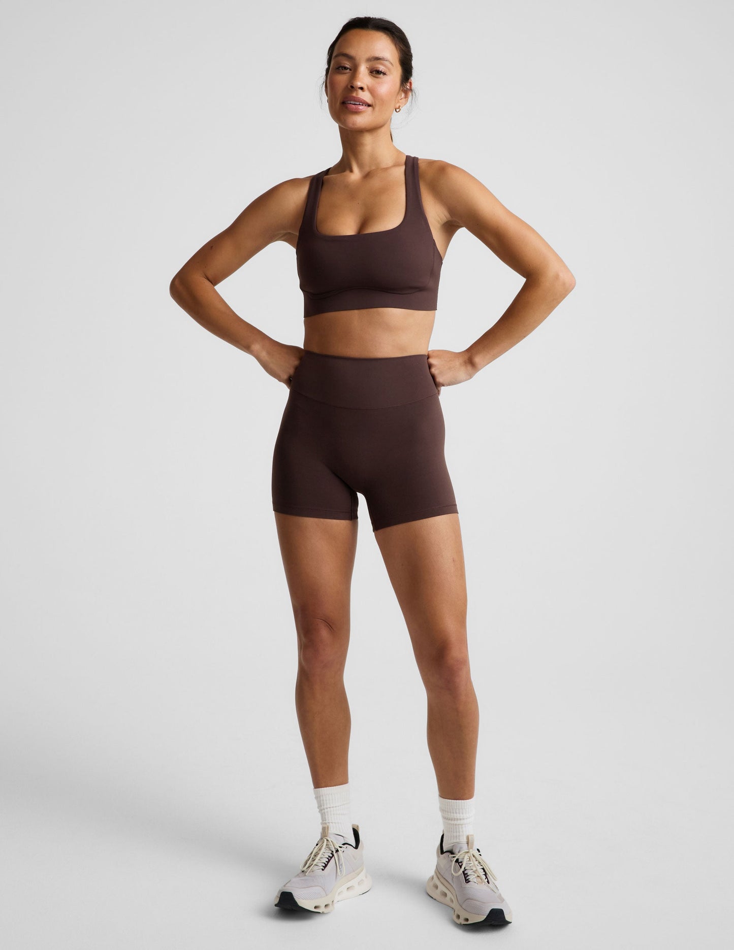 Woman wearing a brown sports bra and brown biker shorts against a plain background.