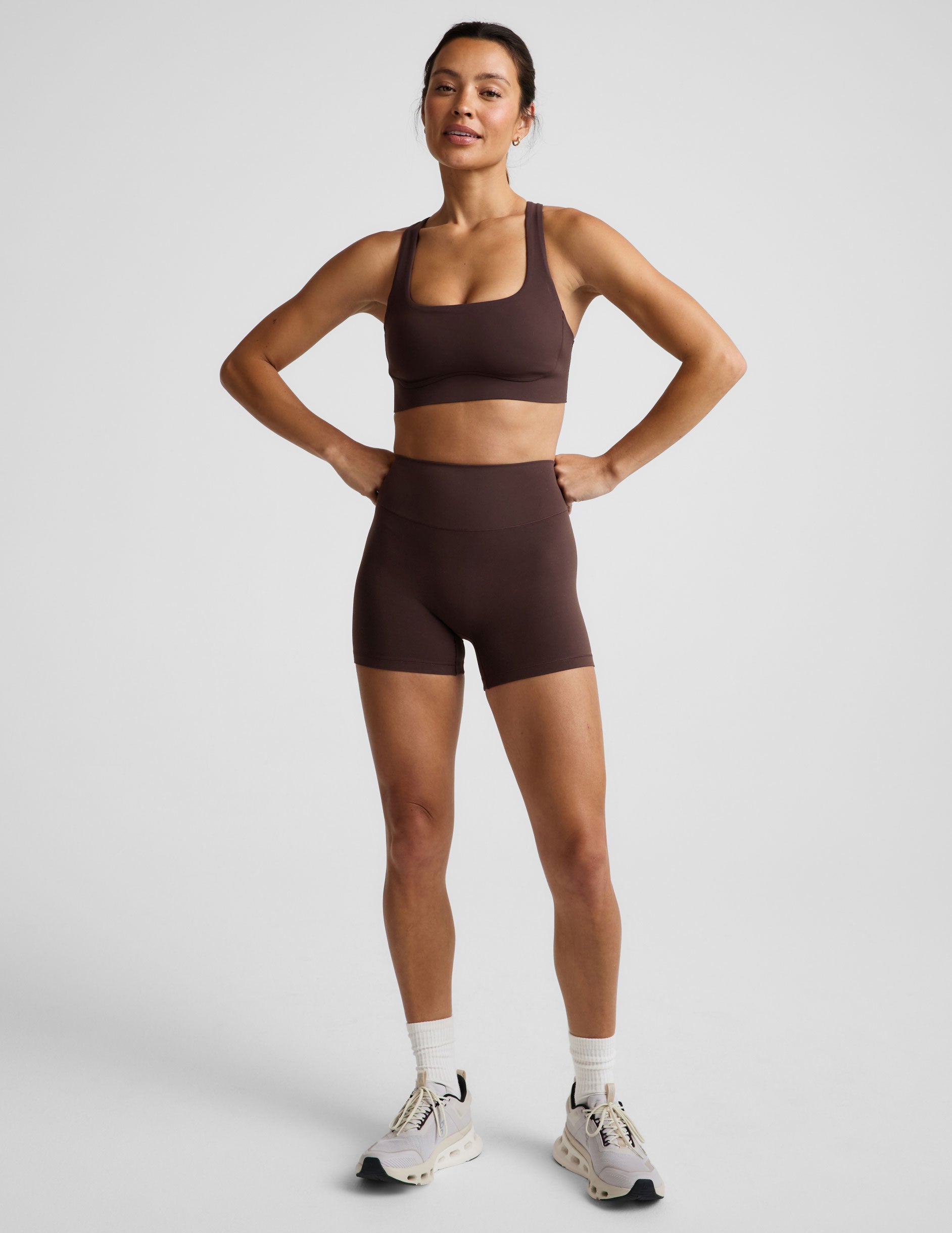 Woman wearing a brown sports bra and brown biker shorts against a plain background.