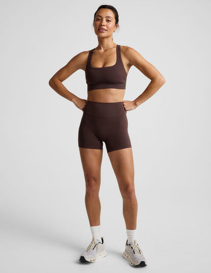 Woman wearing a brown sports bra and brown biker shorts against a plain background.