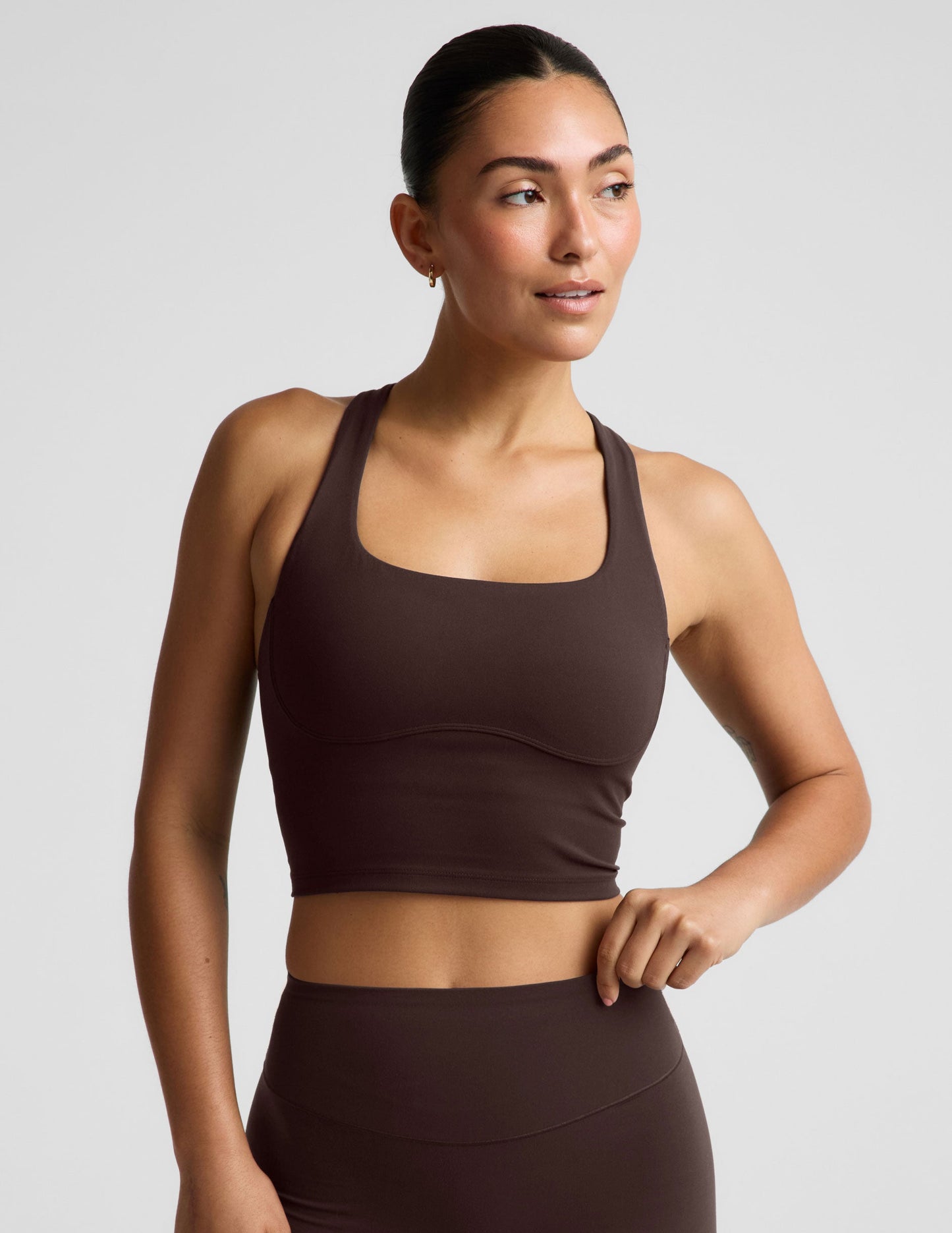 Woman wearing a brown cropped tank and brown midi leggings against a plain background.
