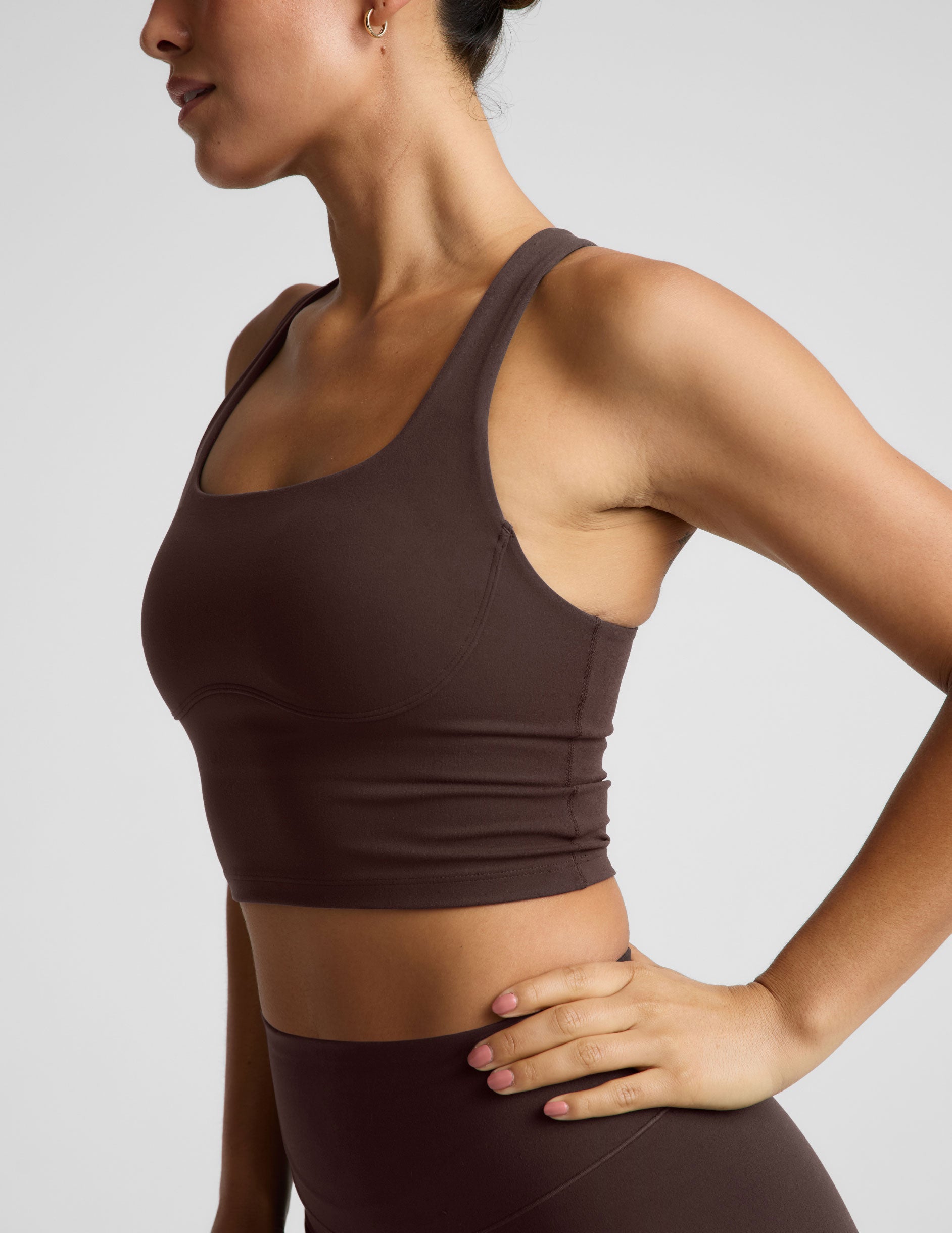 Woman wearing a brown cropped tank and brown midi leggings against a plain background.