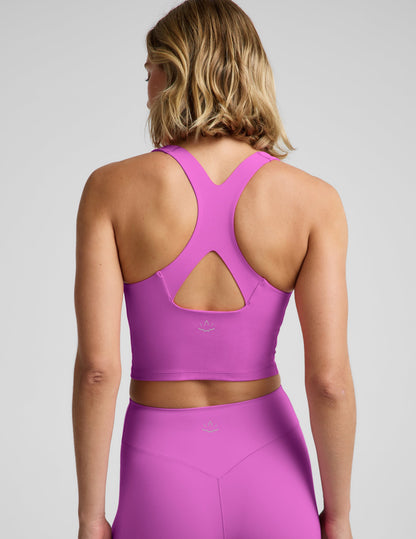 Woman wearing a purple racerback cropped tank and biker shorts against a plain background.
