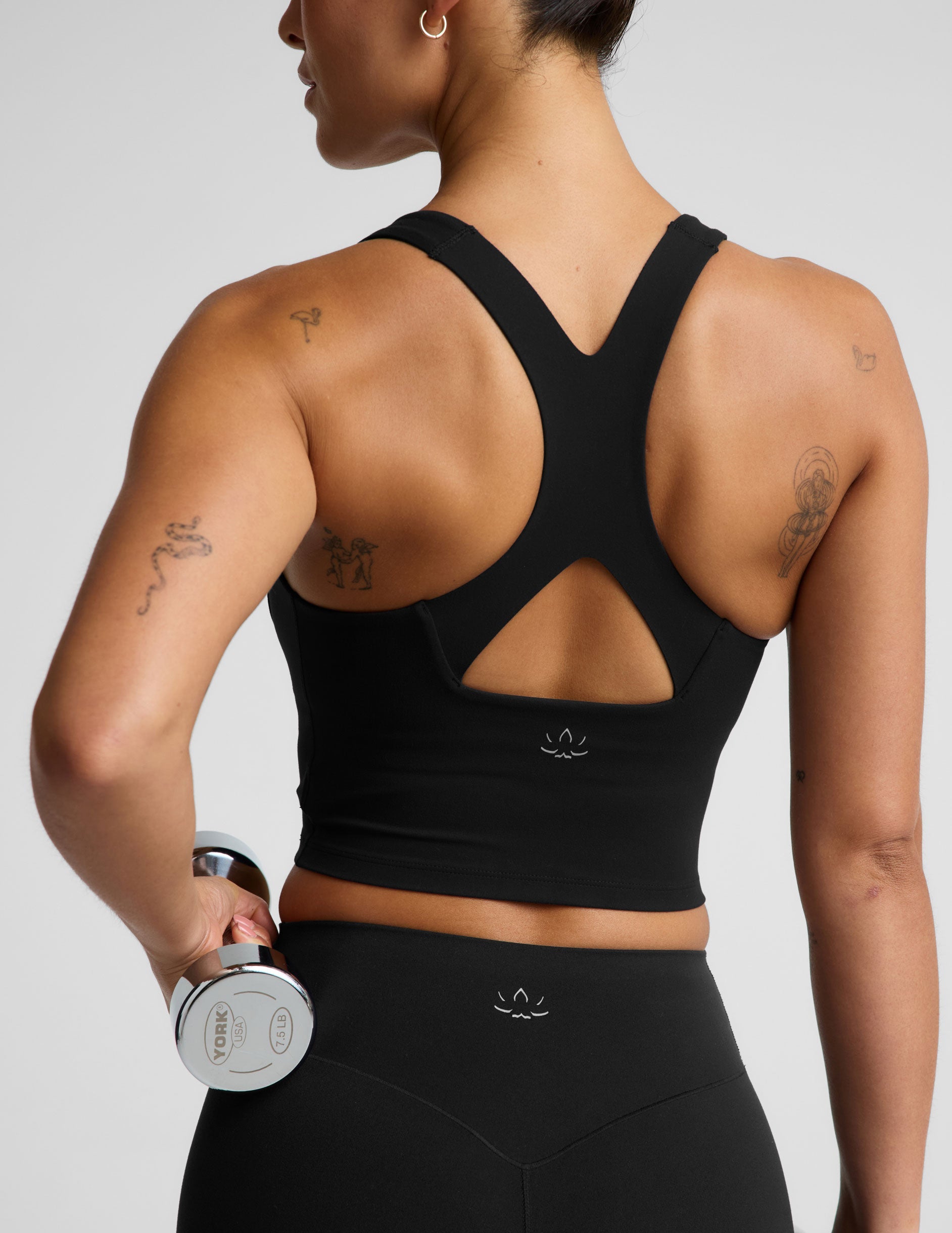 Woman wearing a black cropped tank and biker shorts against a plain studio background.