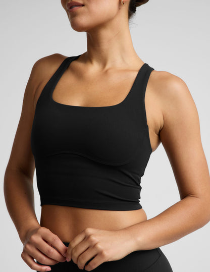 Woman wearing a black cropped tank and biker shorts against a plain studio background.