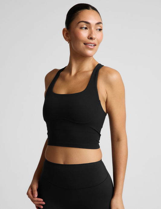 Woman wearing a black cropped tank and biker shorts against a plain studio background.